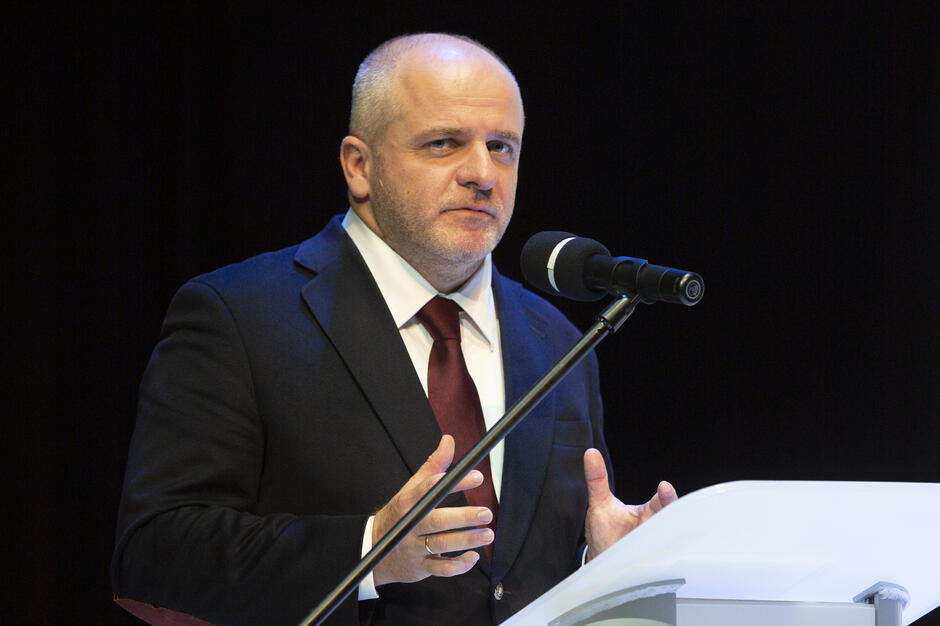 Na zdjęciu widać Pawła Kowala stojącego przy mikrofonie na mównicy konferencyjnej.