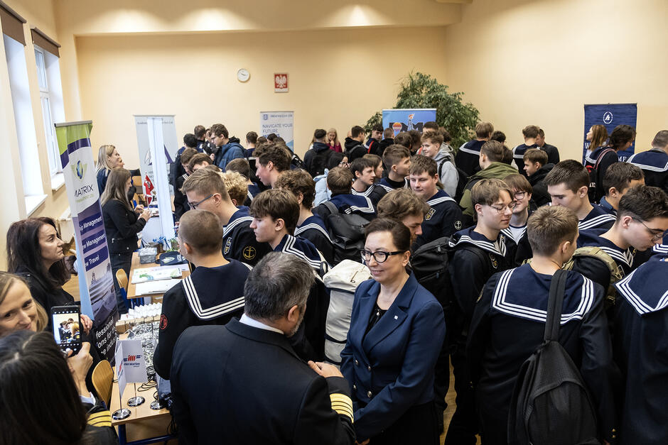 Tłum uczniów w mundurach marynarskich w sali, gdzie stoją stoiska pracodawców.