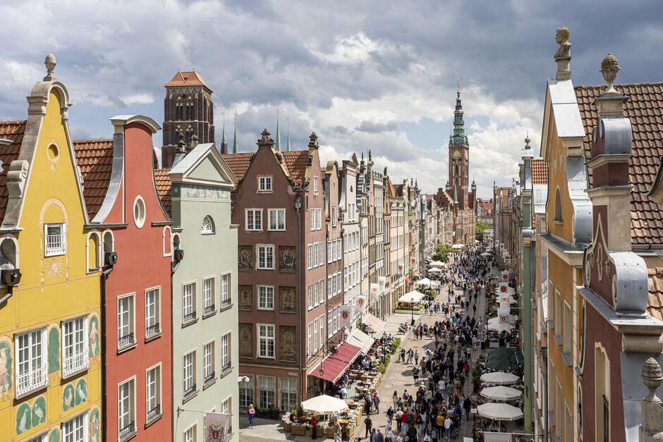 zdjęcie z dachu budynku, widać szczytowe ściany kamienic w gdańsku po środku biegnie deptak po którym idą dziesiątki osób