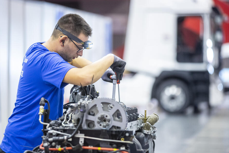 na zdjęciu młody mężczyzna w okularach ochronnych pochyla się nas silnikiem samochodowym