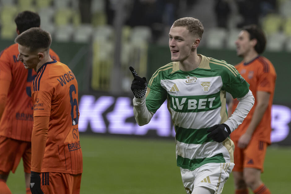 Piłkarz w biało-zielonym stroju po zdobyciu bramki - biegnie uśmiechnięty