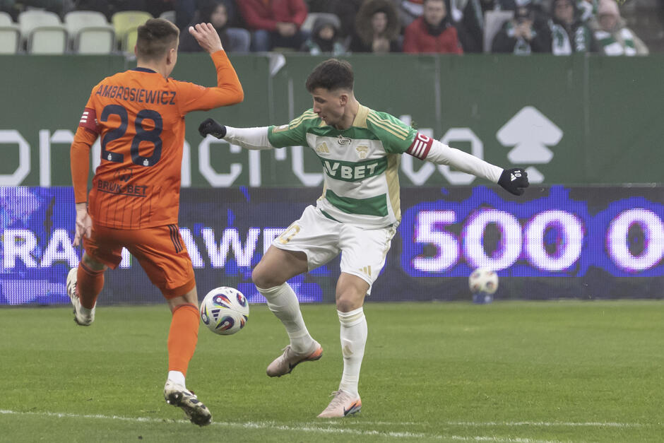 Piłkarz w biało-zielonym stroju przy piłce podczas meczu