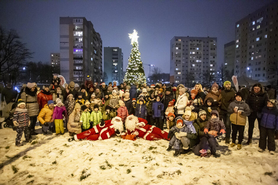 zdjęcie grupowe, przy rozświetlonej choince pozuje ponad trzydzieści osób, w centralnym miejscu na śniegu leży i pozuje dwóch mikołajów w biało czerwonych kostiumach
