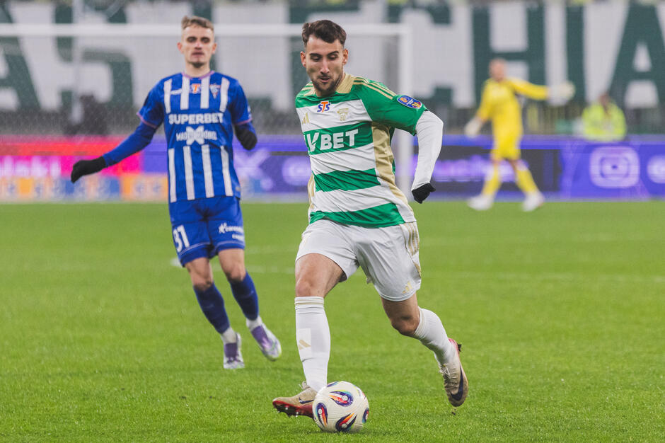 Zawodnik w biało-zielonym stroju, biegnie na boisku przy piłce