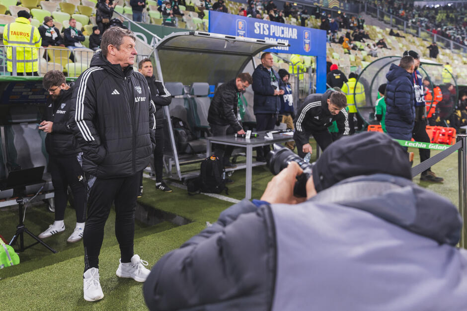 Trener w czarnym dresie podczas meczu - fotoreporterzy robią mu zdjęcia