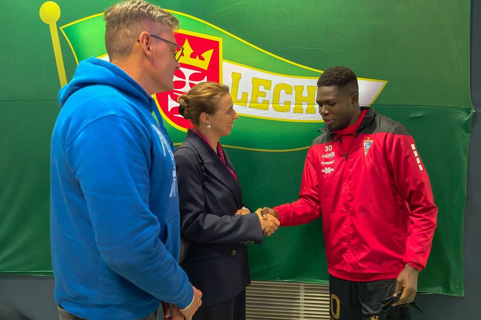 Dwie osoby po lewej w rozmowie z piłkarzem który jest po prawej