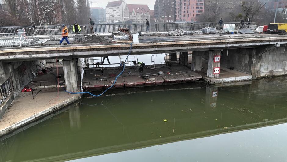 na zdjęciu most widoczny z boku, widać pod nim pracowników pracujących na wodzie na specjalnym pontonie