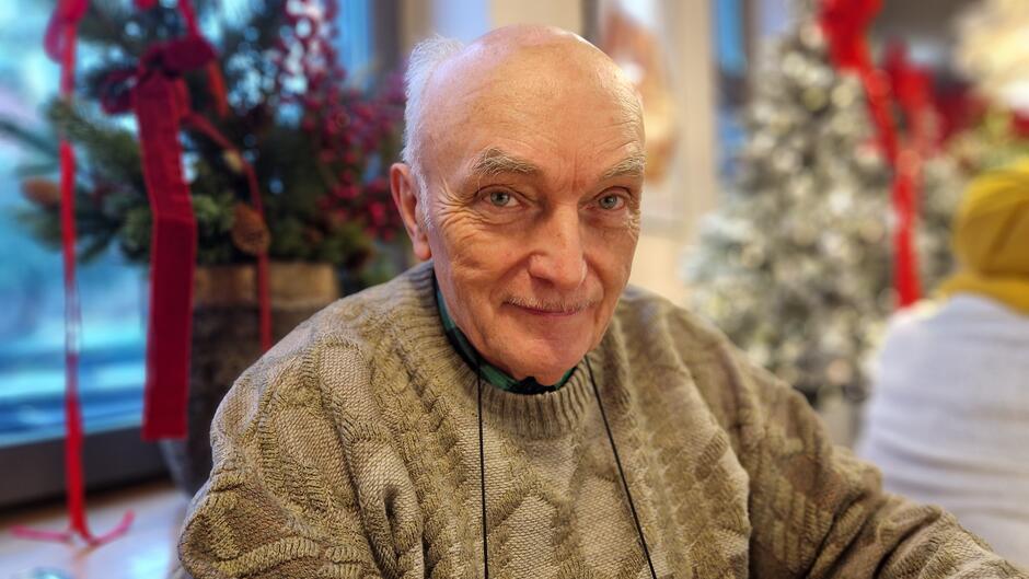 Portret starszego mężczyzny w beżowym swetrze, wśród świątecznej scenerii