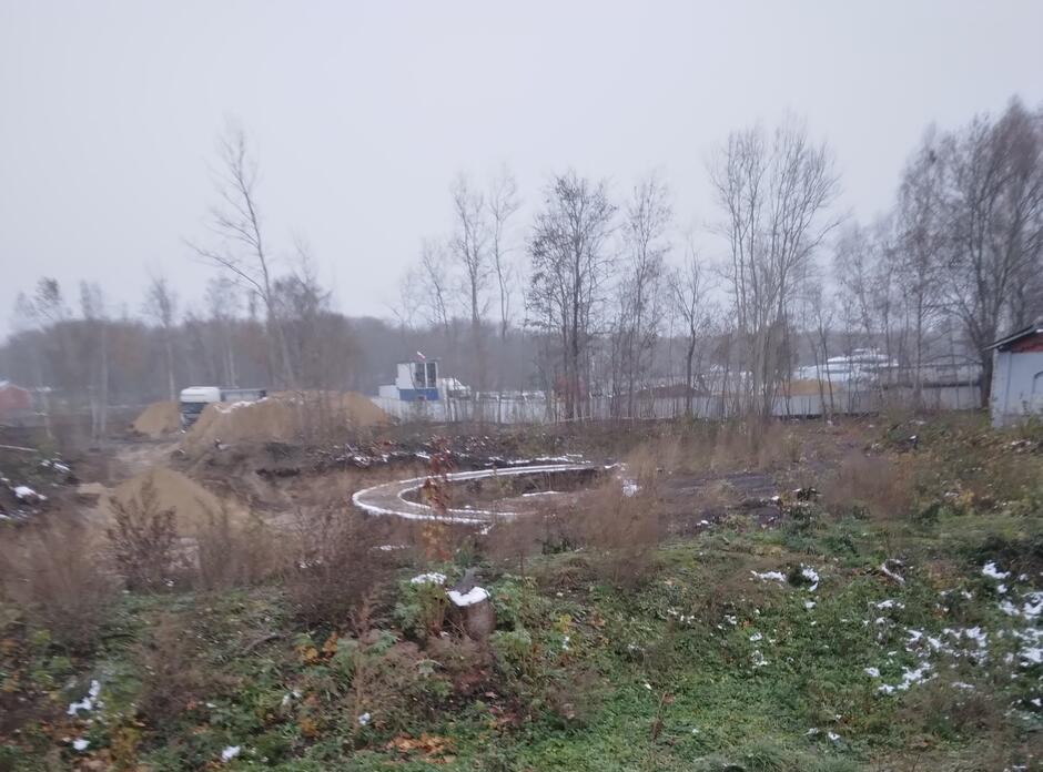 Naokoło trochę drzew, na trawie widoczne resztki śniegu. Pośrodku odkopany ceglany fundament w kształcie okręgu