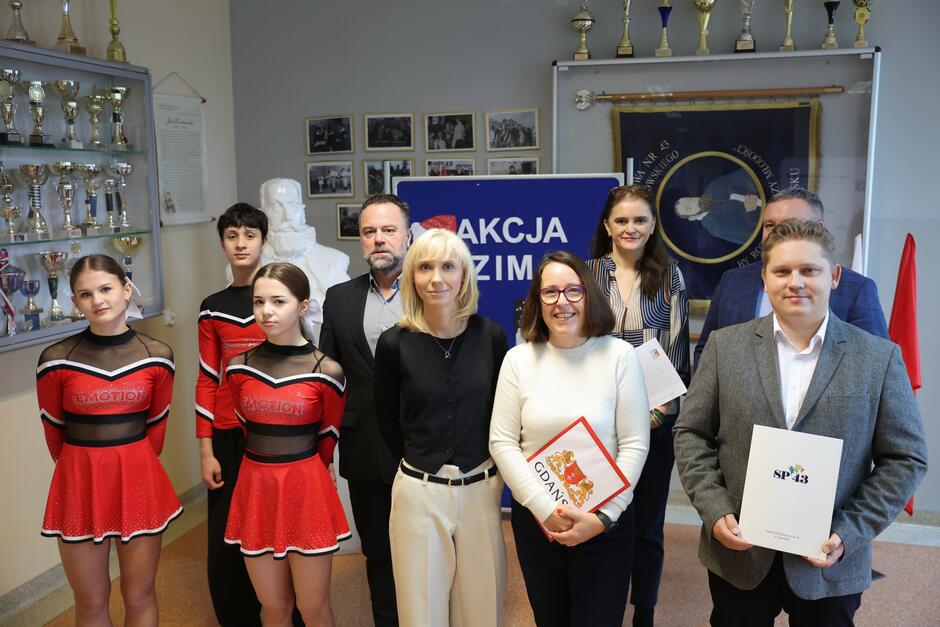 do zdjęcia pozuje pięć dorosłych osób, w oficjalnych strojach, po lewej troje uczniów w strojach sportowych