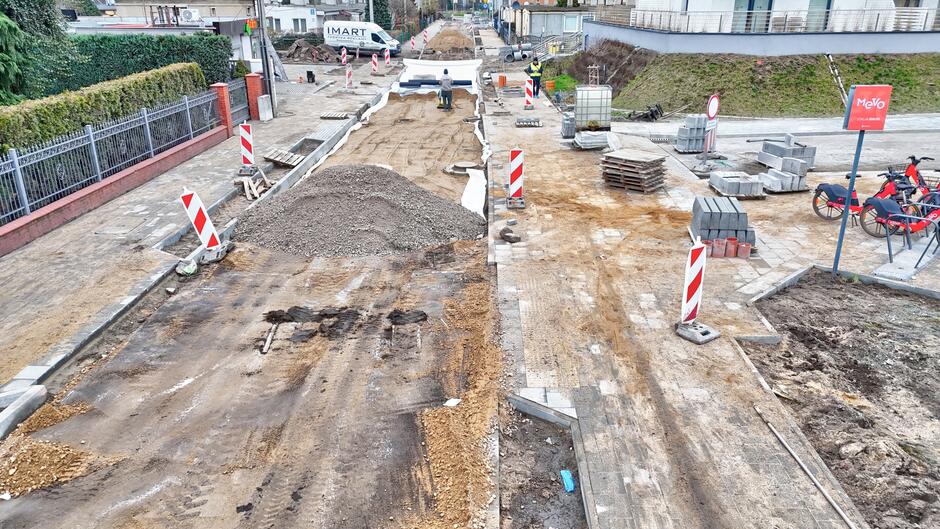 na zdjęciu rozkopana jezdnia, widać też pokryte piaskiem chodniki, po prawej stoi kilka rowerów miejskich w kolorze czerwonym