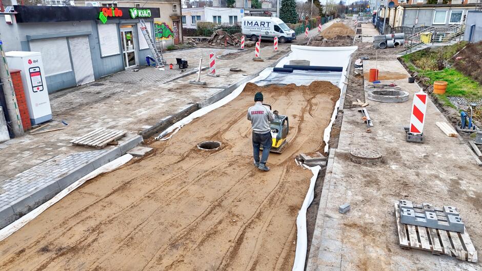 zdjęcie z drona, widać rozkopaną remontowaną ulicę i robotnika ze specjalną maszyną do ubijania piasku