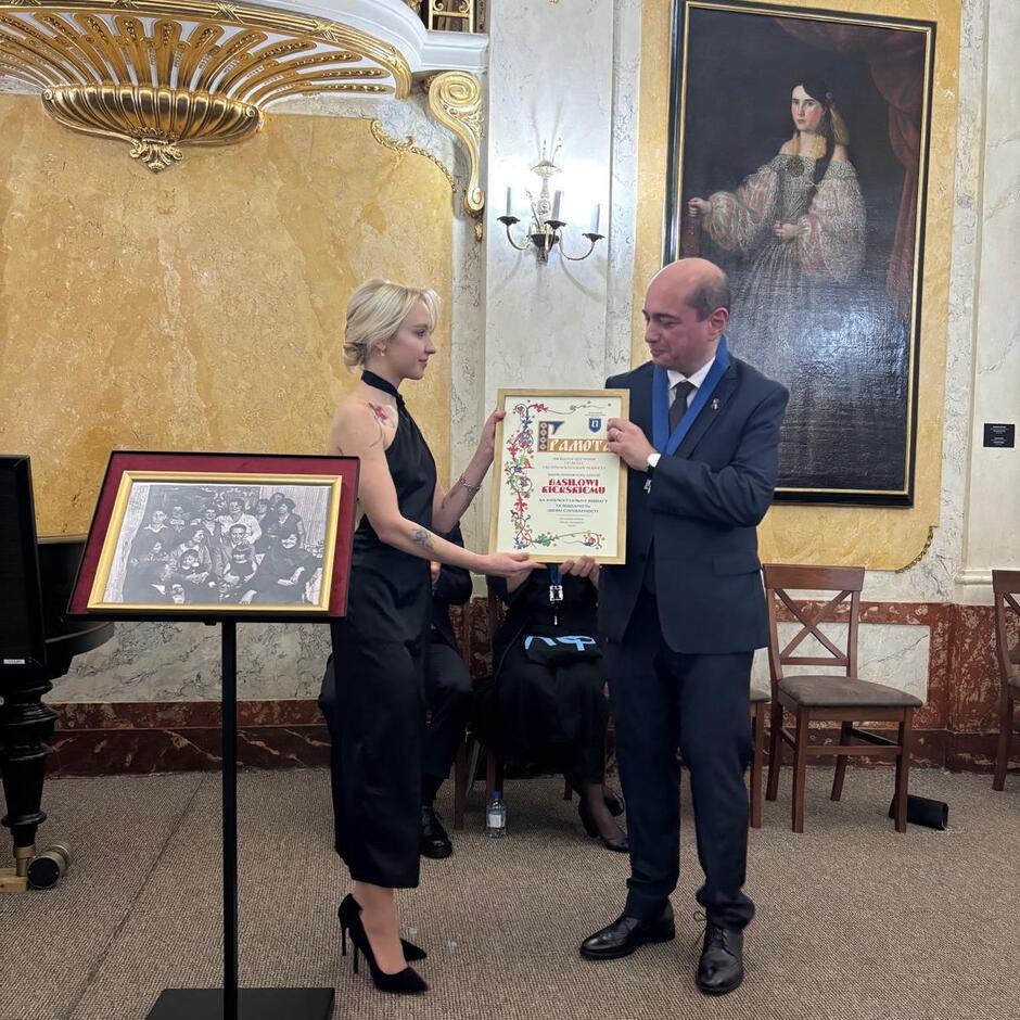 Mężczyzna po prawej przyjmuje dyplom od kobiety która jest po prawej