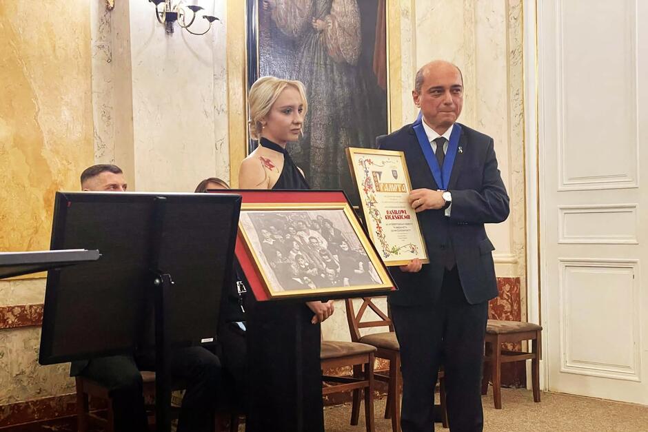 Mężczyzna po prawej przyjmuje dyplom od kobiety która jest po prawej