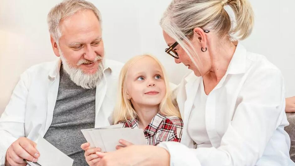 Starsza kobieta i starszy mężczyzna z dziewczynką w wieku lat około 10 - siedzą wszyscy uśmiechnięci dziewczynka między nimi