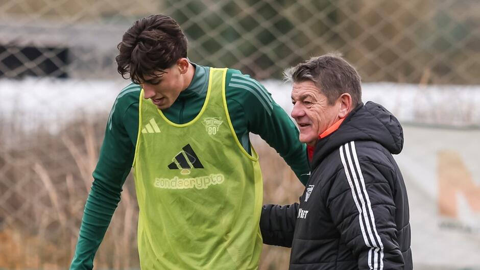 Na pierwszym planie piłkarz z żółtym plastronem i trener podczas treningu piłki nożnej