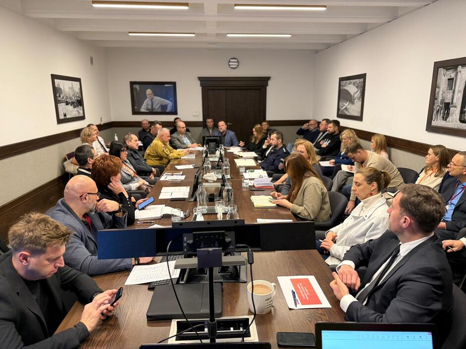 na zdjęciu przy długim dużym, brązowym stole siedzi wokół kilkadziesiąt dorosłych osób