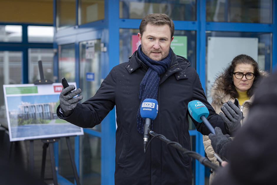 Mężczyzna stoi przed budynkiem i przemawia do mikrofonu.