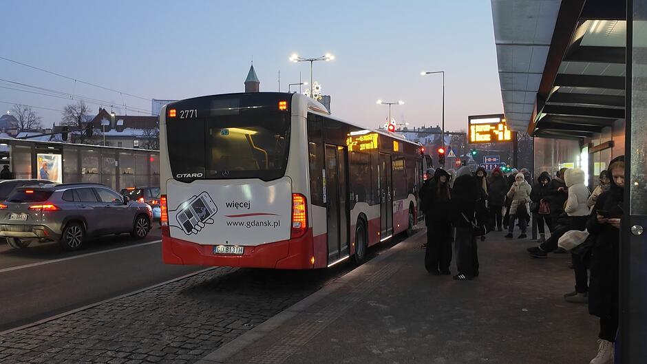 autobus wieczorową, zimową porą odjeżdżający z przystanku. Z tyłu widnieje logotyp gdansk.pl, a na przystanku czekają ludzie