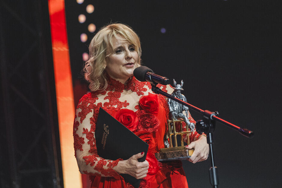 kobieta z nagrodą i dyplomem przemawia do mikrofonu