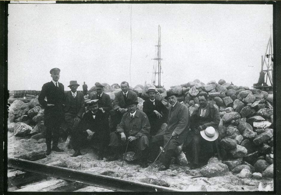 Czarnobiałe zdjęcie, grupa mężczyzn pozuje do zdjęcia na budowie portu.