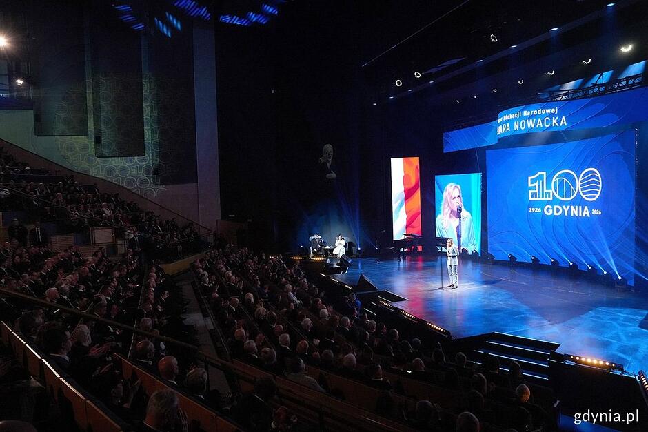 Kobieta na scenie teatru przemawia do mikrofonu.
