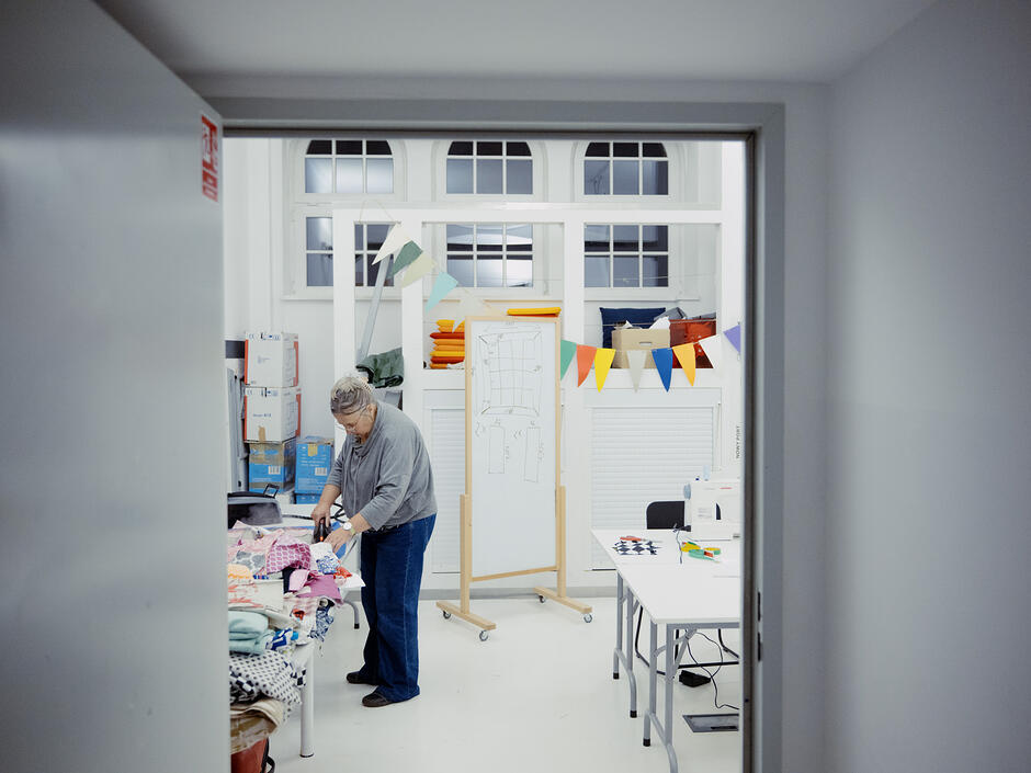 Widok przez uchylone drzwi na kobietę pochyloną nad materiałami