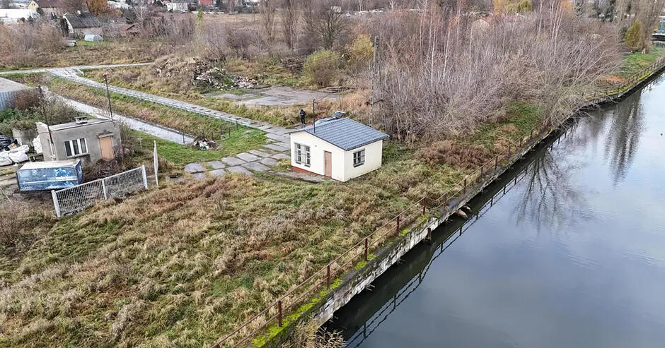 Zdjęcie z lotu ptaka na brzeg rzeki, na którym stoi mały domek. 