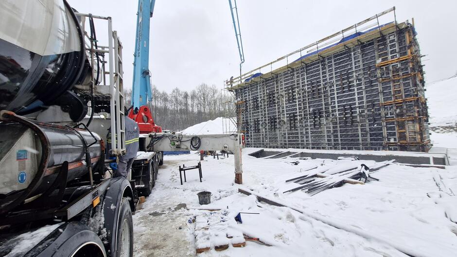 na zdjęciu po prawej powstający przyczółek mostu owinięty czarną folią, po lewej ciężarówka