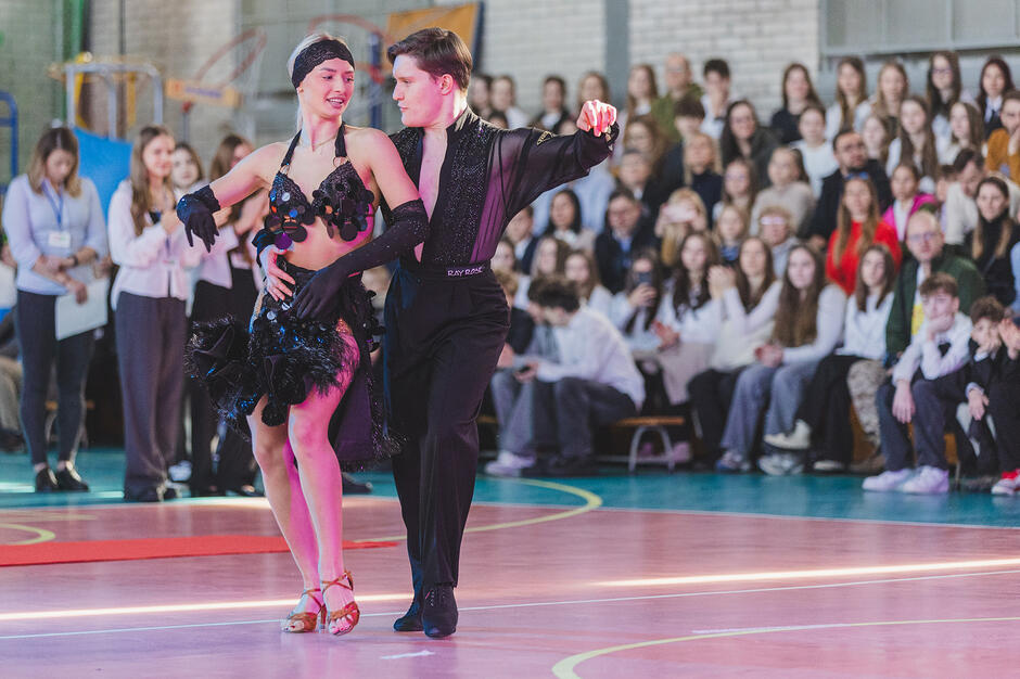 Para młodych ludzi tańczy na hali sportowej.