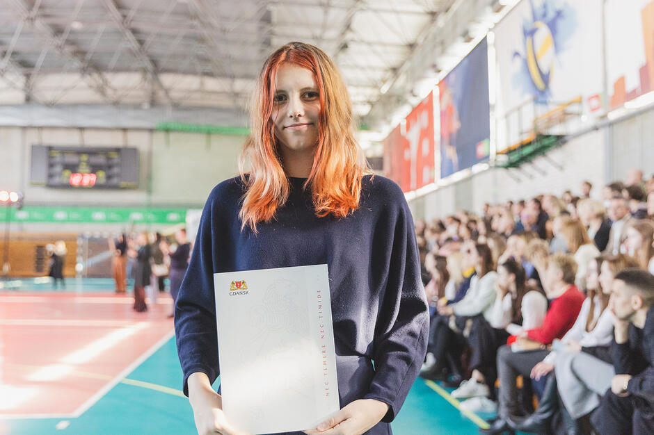 Uczennica pozuje do zdjęcia na hali sportowej.