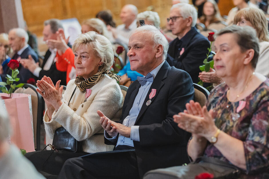 elegancko ubrani seniorzy klaszczą. Mają przy sobie róże i upominki