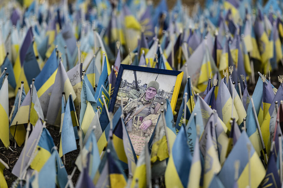 Setki niebieskich chorągiewek - pośród nich zdjęcie jednego z poległych żołnierzy
