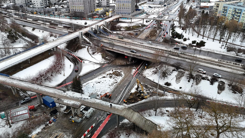 Na zdjęciu widać prace przy rozbiórce starej kładki dla pieszych nad aleją Jana Pawła II na gdańskiej Zaspie. W zimowej scenerii widoczne są koparki oraz fragmenty konstrukcji nad jezdniami i torowiskiem tramwajowym, co wiąże się z wprowadzeniem tymczasowej organizacji ruchu w tym rejonie.
