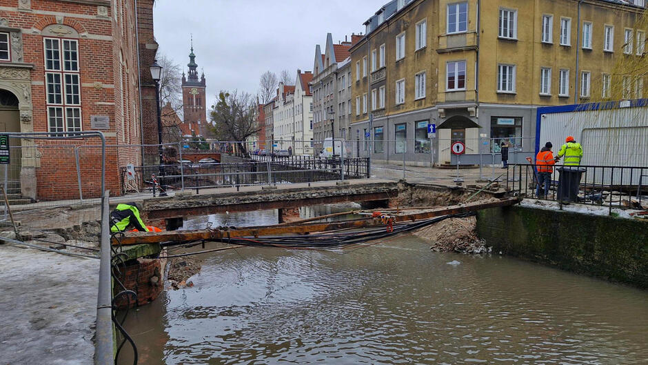 na zdjęciu rzeka, nad którą zwisają sieci, w tle kamienice po obu stronach ulicy