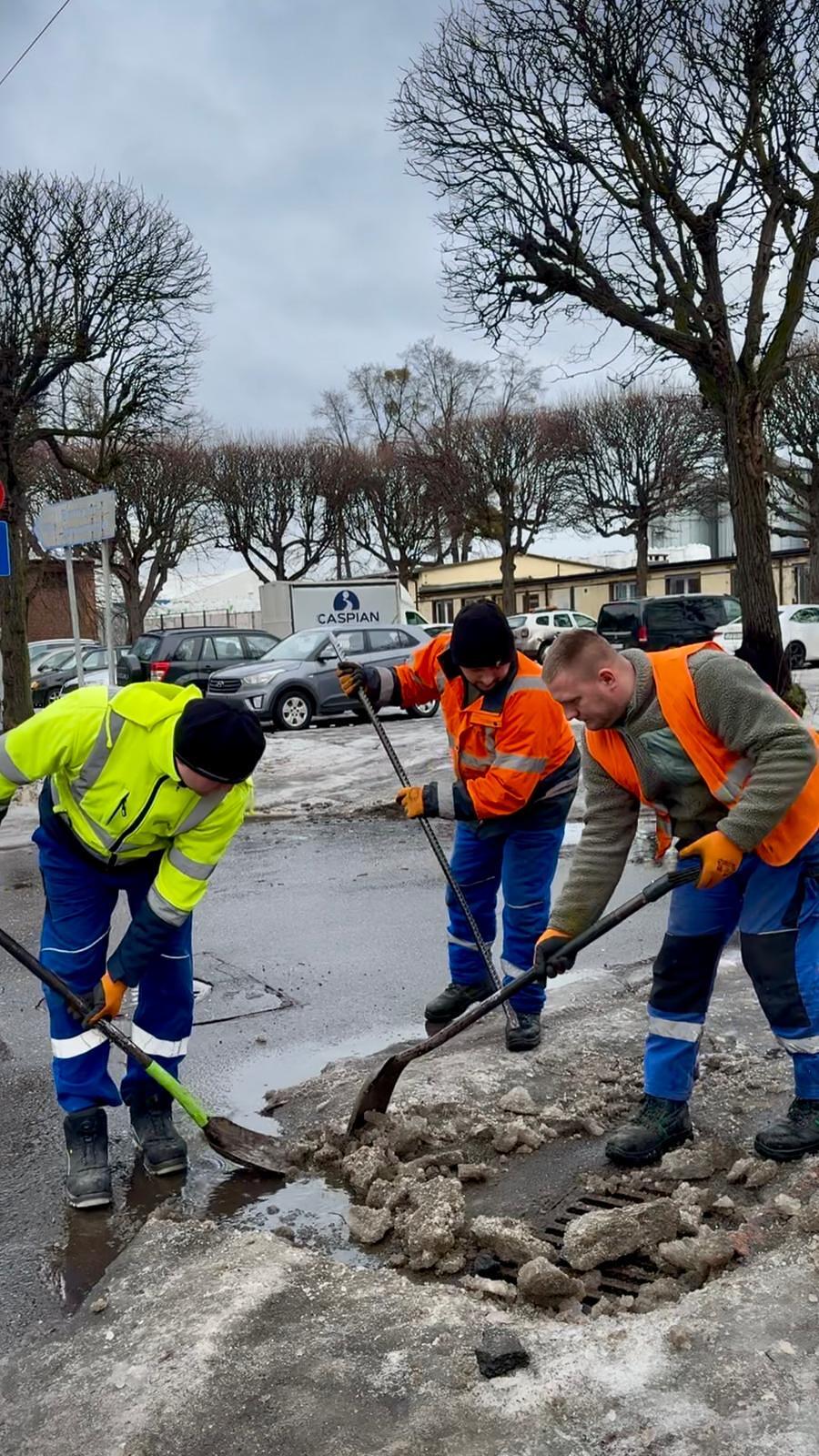 trzech robotników w jaskrawych kamizelkach odśnieża łopatami ulicę