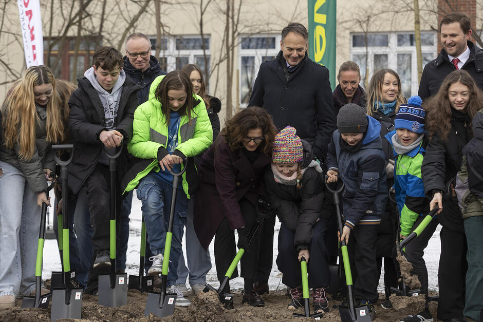 Grupa osób wbija łopaty w ziemię na budowie.