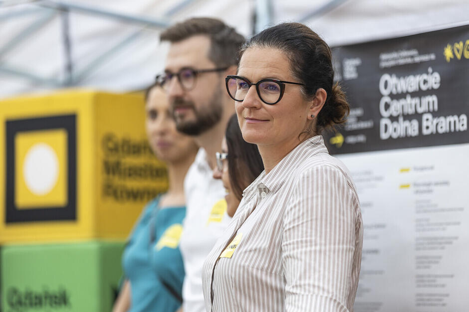 na pierwszym tle kobieta w jasnej koszuli w pomieszczeniu i w okularach. W tle mężczyzna, również w okularach