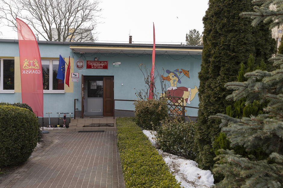 Na zdjęciu widać budynek. Przed wejściem do błękitnego obiektu rozciąga się chodnik z kostki brukowej, a elewację zdobi kolorowy malunek kaczora w kapeluszu.
