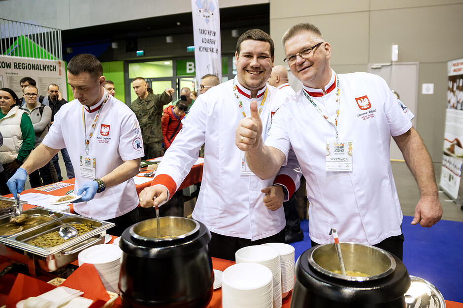 Kucharze przy garnkach na hali targowej, uśmiechają się i pozują do zdjęcia.