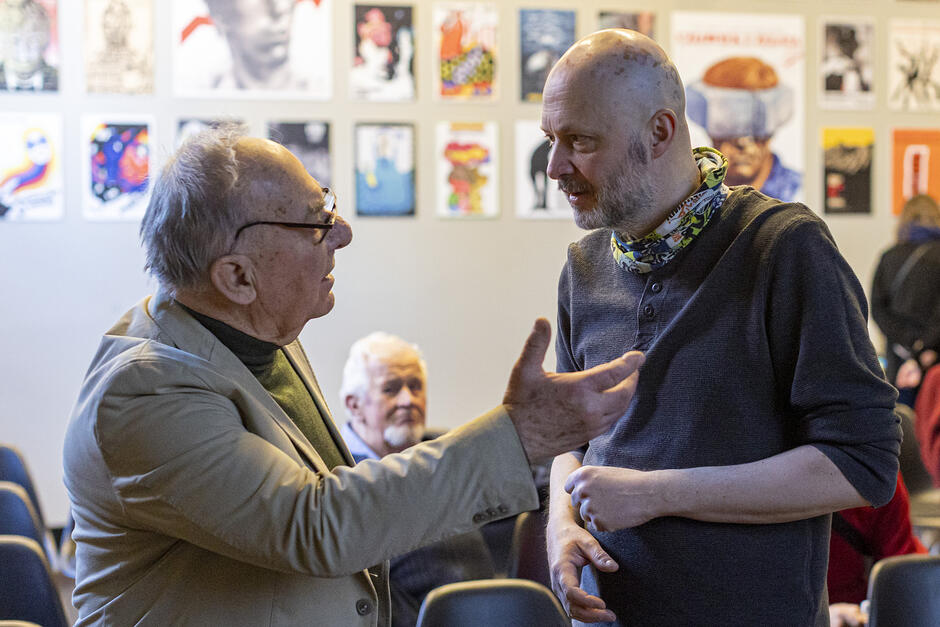 Dwaj mężczyźni stoją rozmawiając - ten po lewej w wieku senioralnym - po prawej w średnim wieku