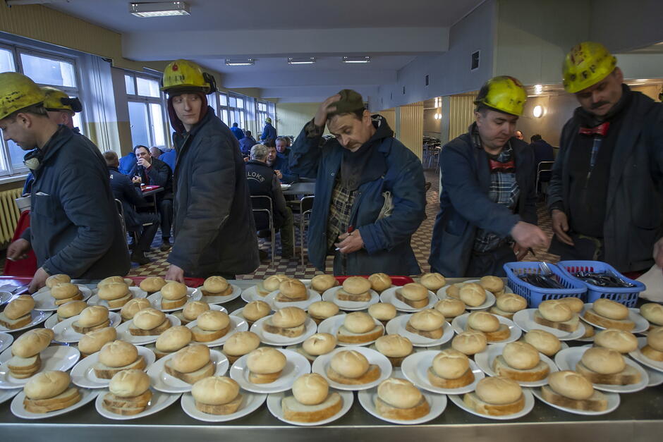 robotnicy stoją w stoczniowej stołówce. Przed nimi - na talerzach - porcje pieczywa