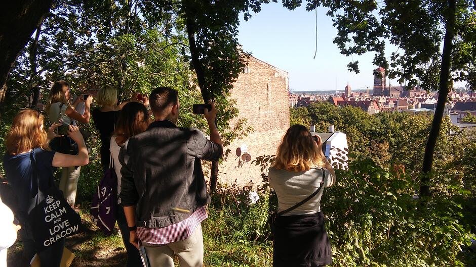 Grupa ludzi z telefonami skierowanymi w stronę panoramy Głównego Miasta w Gdańsku