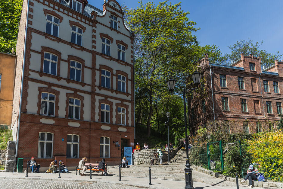 Grupa ludzi siedzących i rysujących w różnych miejscach na zakręcie ulicy Biskupiej