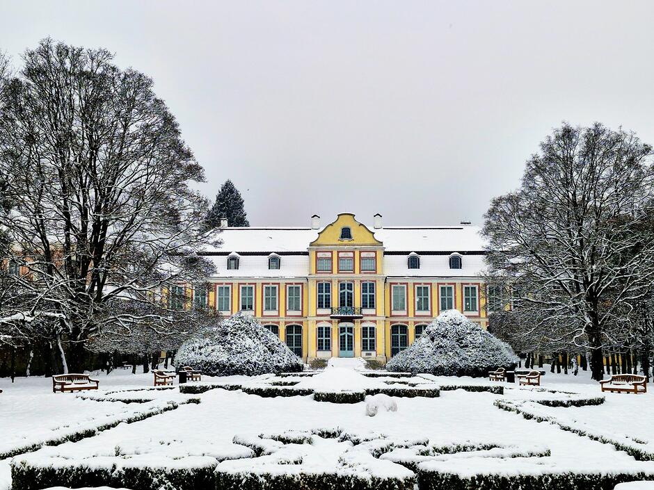 Park zimą, przykryte śniegiem klomby, drzewa i pałac.