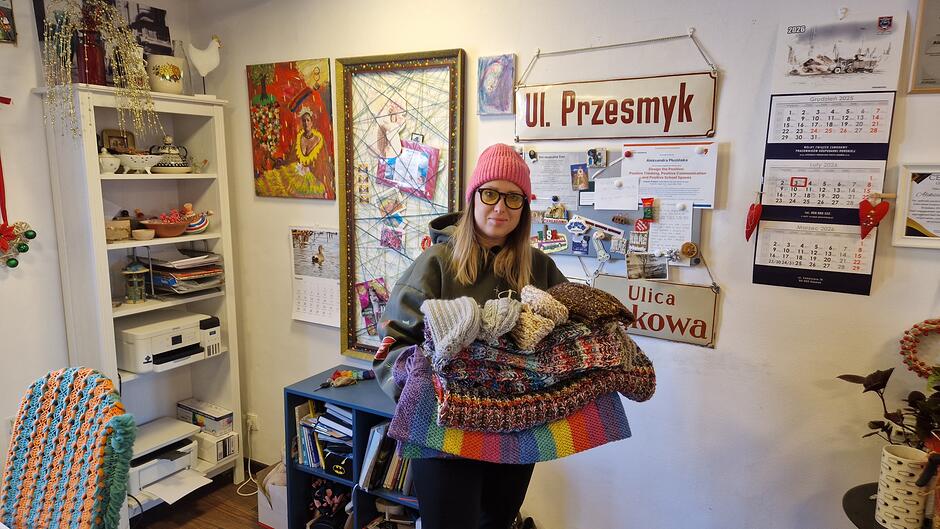 Dziewczyna w różowej wełnianej czapce i okularach z naręczem czapek i szalików