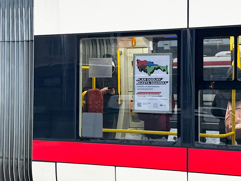 kremowo czerwony tramwaj od zewnątrz, na którego oknie widnieje plakat