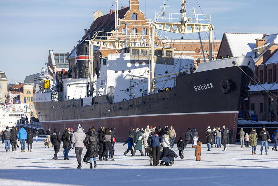 Statek Sołdek  na zamarzniętej rzece Motławie, po której spacerują tłumy ludzi.