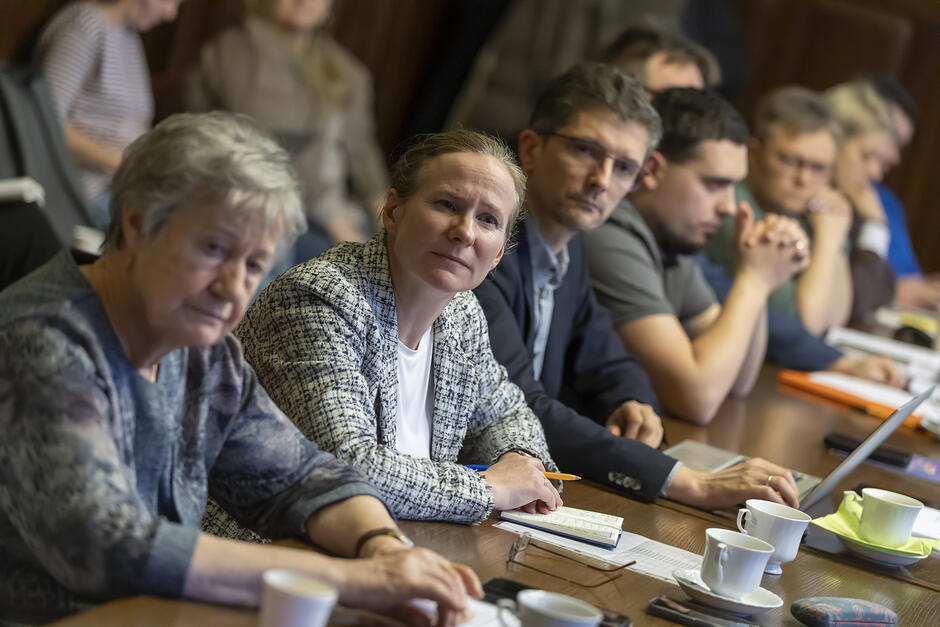 na zdjęciu kilka osób w średnim wieku, siedzi przy dużym brązowym stole, patrzą przed siebie