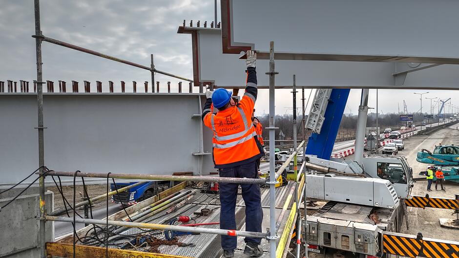 na zdjęciu robotnik w białym kasku trzymający duże stalowe elementy wiaduktu